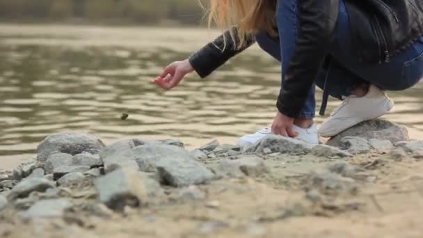 Ženská ruka hodí kámen do vody na břehu řeky. — Stock video