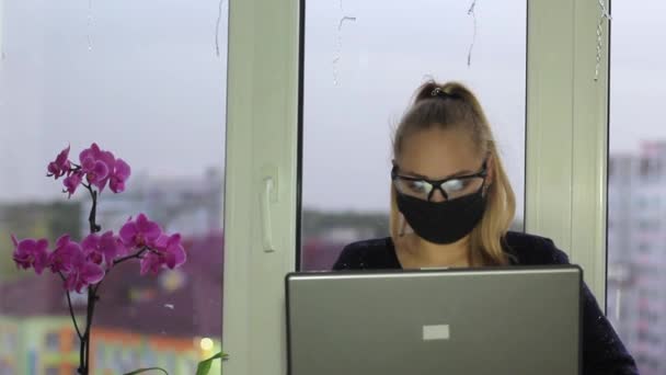 이 프리랜서 소녀는 의료용 마스크와 안경을 쓰고 코로나 바이러스가 유행하는 동안 노트북에서 일 한다. — 비디오