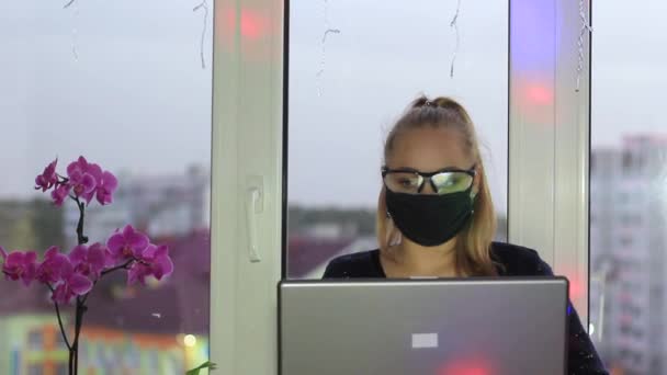 Zelfisolatie freelancer meisje dat werkt op een laptop tijdens een epidemie. De achtergrond is gemarkeerd met kleurrijke bloemen. — Stockvideo