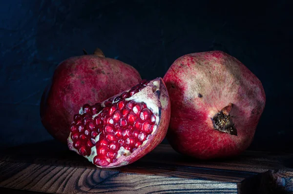 Granadas, frutas sabrosas y maduras sobre fondo negro, sobre tabla de cortar, estilo rústico — Foto de Stock