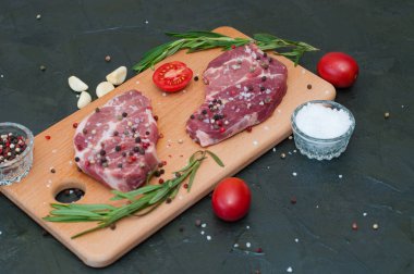 Kesme tahtasındaki çiğ et, tuz ve biber serpilmiş, sarımsak, biberiye ve domates, üst görüş ve yan görüş.