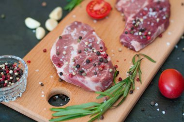 Kesme tahtasındaki çiğ et, tuz ve biber serpilmiş, sarımsak, biberiye ve domates, üst görüş ve yan görüş.