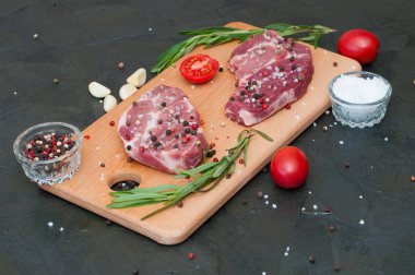 Kesme tahtasında çiğ et, tuz ve biber serpiştirilmiş, sarımsak, biberiye ve domates, üst görüş ve yan görüş.