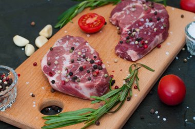 Kesme tahtasında çiğ et, tuz ve biber serpiştirilmiş, sarımsak, biberiye ve domates, üst ve yan görünüm.