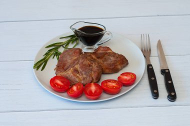 Sos, biberiye ve domatesli gri bir tabakta hafif ahşap arka planda leziz domuz bifteği.