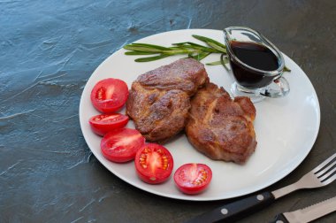 Fragrant pork steaks with spices, tomatoes and sauce, on a gray plate, on dark background with place for text
