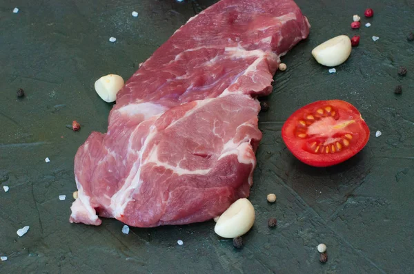 Vaření vepřový steak, maso posypané solí a pepřem, stroužky česneku a plátky rajčat na šedém betonovém pozadí, pohled shora a ze strany — Stock fotografie