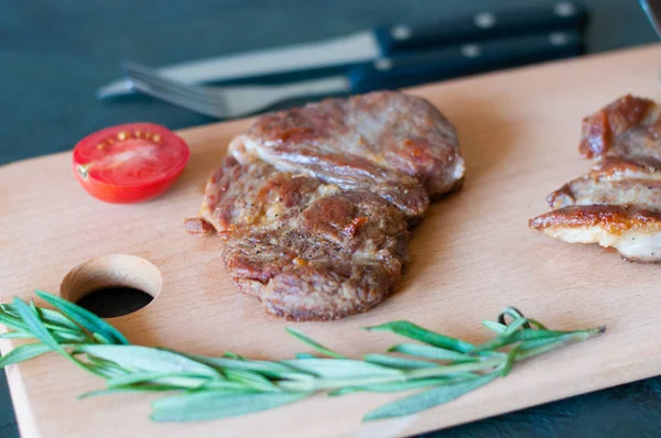 Grilovaný masový steak z vepřového, telecího nebo hovězího masa, s rozmarýnem, sójovou omáčkou a rajčaty na řezací desce, vidličkou a nožem, zblízka, shora a z boku — Stock fotografie