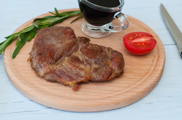 Filete frito, delicioso de ternera, ternera o cerdo, tomate, romero y salsa de soja para carne en una tabla redonda de madera, sobre un fondo claro, cuchillo y tenedor, primer plano —  Fotos de Stock