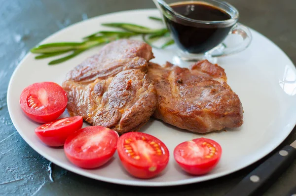 Fragrant pork meat steaks with spices, tomatoes and sauce, on a gray plate, on dark concrete background with place for text — Stock Photo, Image