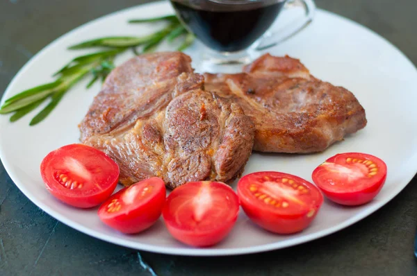 Voňavé vepřové steaky s kořením, rajčaty a omáčkou, na šedém talíři, na tmavém betonovém pozadí s místem pro text — Stock fotografie