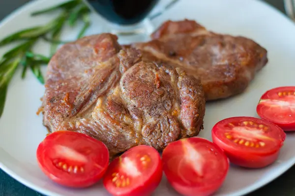 Illatos sertéshús steak fűszerekkel, paradicsommal és szósszal, szürke tálcán, sötét beton alapon, közelkép — Stock Fotó