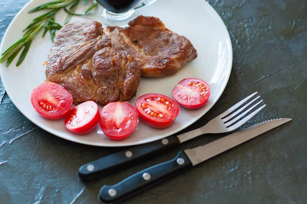 Szaftos hússteak borjúból, marhahúsból vagy sertéshúsból rozmaringgal, paradicsommal és szósszal, szürke alapon, sötét betonalapon, fénymásoló felülettel — Stock Fotó