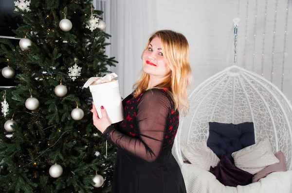 Exuberante, bela, jovem mulher perto da árvore de Natal com um presente, esperando o feriado — Fotografia de Stock