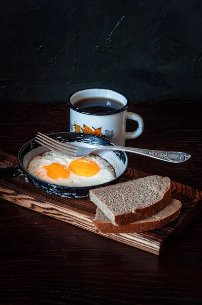 Fried scrambled eggs in a vintage pan, with bread, metal mug with tea — Stock Photo, Image