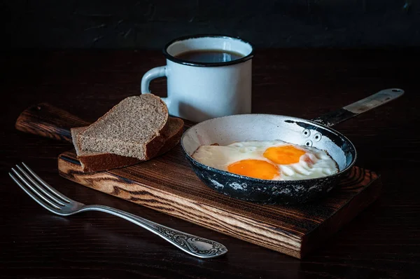 Gebratene Rührei in Vintage-Pfanne, mit Brot, alter Gabel, Metallbecher mit Tee, Seitenansicht, dunkler Hintergrund — Stockfoto