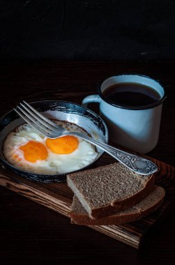 Eski bir tavada çırpılmış yumurta, ekmek, çay ve metal bardak.