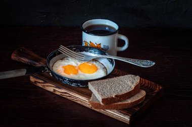 Eski bir tavada çırpılmış yumurta, ekmek, çay ve metal bardak.
