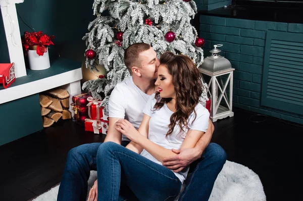 Liebendes Paar, Mann und Frau, kuscheln und schauen sich im neuen Jahr in der Nähe von Weihnachtsbaum und Kamin an — Stockfoto