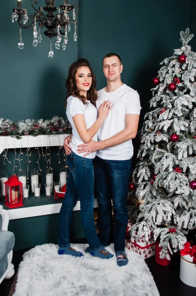 Pareja cariñosa, hombre y mujer, mimándose en el interior de Año Nuevo cerca del árbol de Navidad y la chimenea —  Fotos de Stock