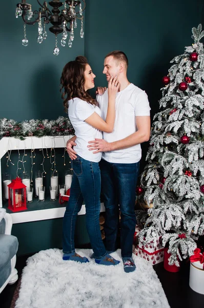 Casal amoroso, marido e mulher, homem e mulher, abraçar e olhar um para o outro no interior do Ano Novo perto da árvore de Natal e lareira — Fotografia de Stock