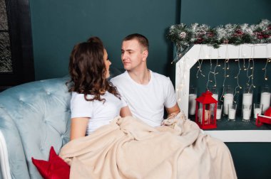 Sevgi dolu evli bir çift, zayıf, atletik bir erkek ve şöminenin yanındaki kanepede güzel bir kadın. Ekoseye sarılı oturan çift.