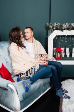 Sevgi dolu evli bir çift, zayıf, atletik bir erkek ve şöminenin yanındaki kanepede güzel bir kadın. Ekoseye sarılı oturan çift.