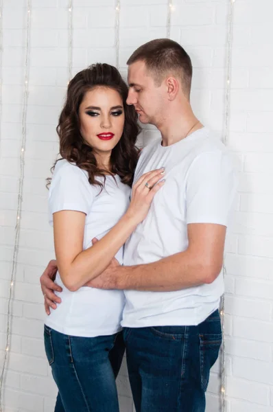 Joven hermosa pareja enamorada cerca de la guirnalda de Año Nuevo en la pared blanca en el estilo loft —  Fotos de Stock