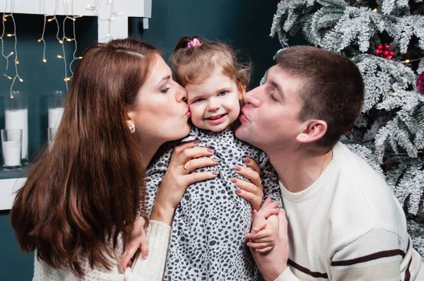 Amare coppia sposata, bell'uomo e bella donna vicino all'albero di Natale, baciare la loro piccola figlia sulle guance — Foto Stock