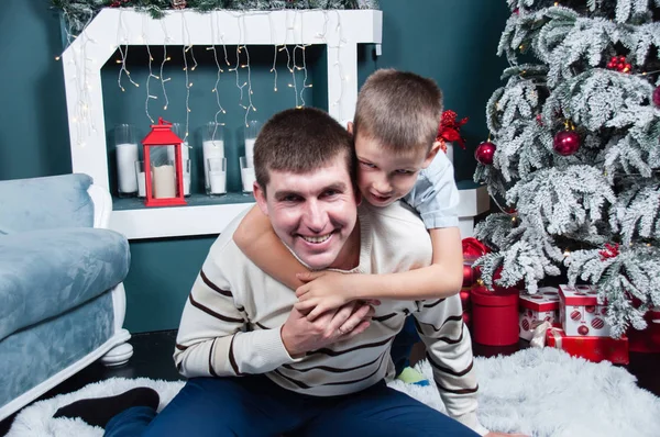 Padre e figlio si dilettano, giocano vicino all'albero di Natale, al camino e ai regali . — Foto Stock
