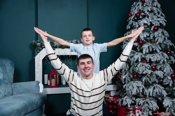 Padre e figlio si dilettano, giocano vicino all'albero di Natale, al camino e ai regali . — Foto Stock