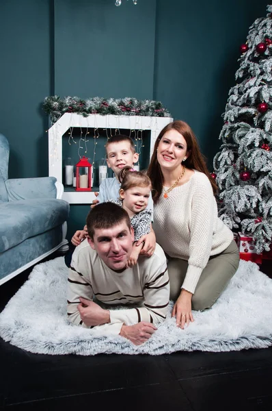 Famiglia, genitori e due bellissimi bambini, ragazzo e una ragazza, si divertono a giocare vicino al camino e all'albero di Natale sul divano — Foto Stock