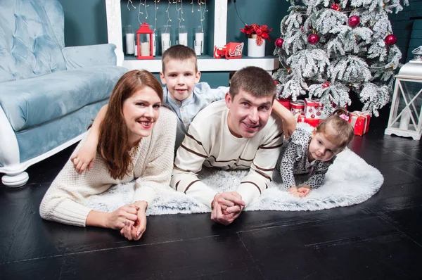 Famiglia, genitori e due bambini, ragazzo e una ragazza, sorridenti, che si divertono vicino al camino di un albero di Natale sul tappeto — Foto Stock