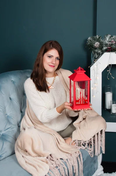 Mulher muito bonita, feliz, misteriosamente sorridente sentada perto da lareira Árvore de Natal. Posando com uma lanterna decorativa em suas mãos, olhando para a câmera — Fotografia de Stock