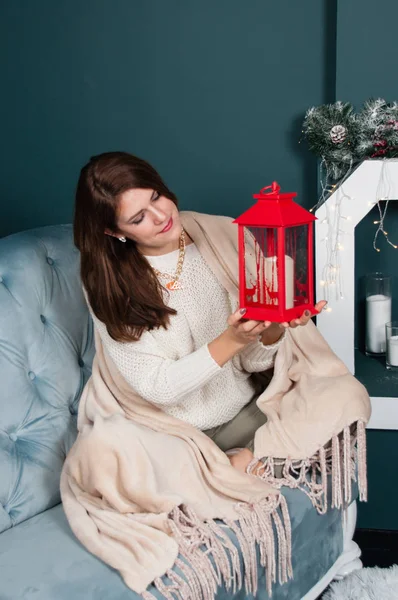 Mulher muito bonita, feliz, misteriosamente sorridente sentada perto da lareira Árvore de Natal. Posando com uma lanterna decorativa em suas mãos — Fotografia de Stock