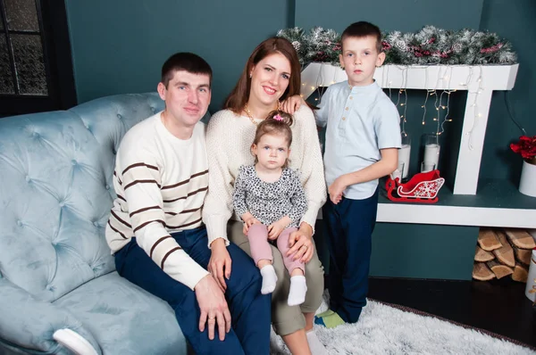 Famille, parents et deux beaux enfants, garçon et fille, près de la cheminée et l'arbre de Noël sur le canapé — Photo