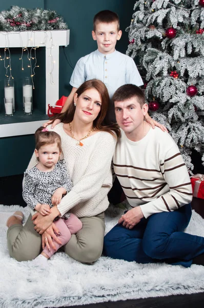 Familj, föräldrar och två barn, en pojke och en flicka, leende, ha kul nära eldstaden i en julgran — Stockfoto