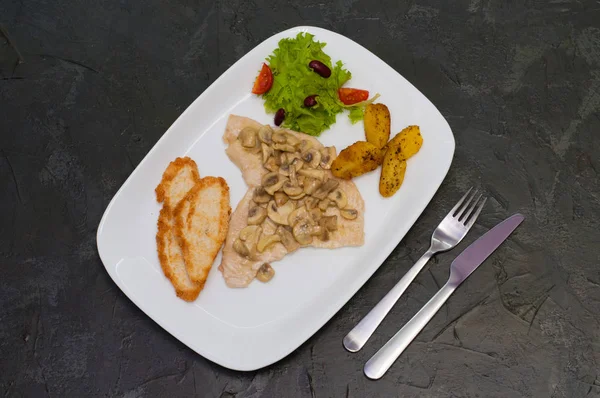 Setas guisadas con filete de pescado, ensalada, papas fritas y croutons, sobre un fondo gris cálido. Sabrosa comida italiana tradicional —  Fotos de Stock