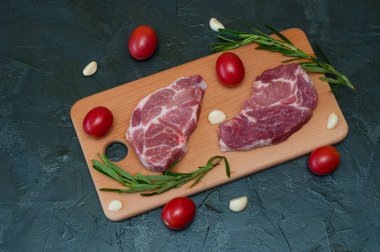 Domatesli çiğ domuz bifteği, sarımsak ve ahşap bir tahtada biberiye.