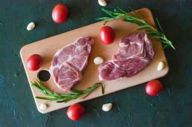 Domatesli çiğ domuz bifteği, sarımsak ve biberiye ahşap kesim tahtasının üstünde.