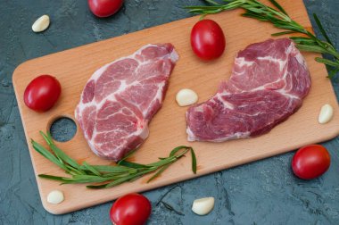 Düz yatıyordu, çiğ et iki domuz bifteği domatesli sarımsak ve biberiyeli ahşap kesim tahtasına yakın çekim.