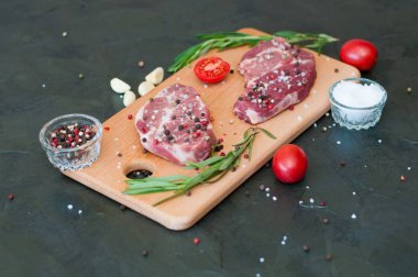 Kesme tahtasında çiğ et, tuz ve biber serpiştirilmiş, sarımsak, biberiye ve domates, üst görüş ve yan görüş.