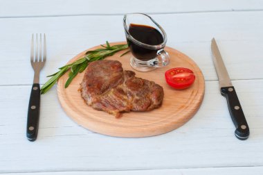 Kızarmış, lezzetli dana eti, biftek ya da domuz eti, domates, biberiye ve soya sosu yuvarlak ahşap tahtada, hafif arka planda, bıçak ve çatal üzerinde.