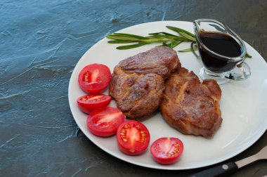 Fragrant pork steaks with spices, tomatoes and sauce, on a gray plate, on dark background with place for text