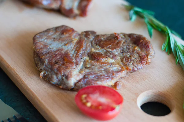 Grilovaný masový steak z vepřového, telecího nebo hovězího masa, s rozmarýnem, sójovou omáčkou a rajčaty na řezací desce, vidličkou a nožem, zblízka, shora a z boku — Stock fotografie