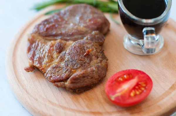 Vařený grilovaný vepřový steak na dřevěné kulaté desce se sójovou omáčkou, rozmarýnem a rajčaty — Stock fotografie