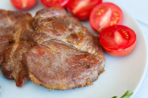 Schmackhafte, saftige, gebratene Steaks von Schwein oder Rind mit Sauce, Gewürzen und Tomaten auf grauem Teller, auf hellem Holzgrund, Draufsicht — Stockfoto