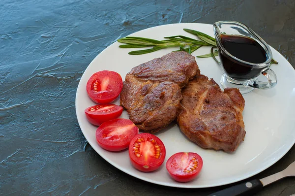 Fragrant pork steaks with spices, tomatoes and sauce, on a gray plate, on dark background with place for text — Stock Fotó