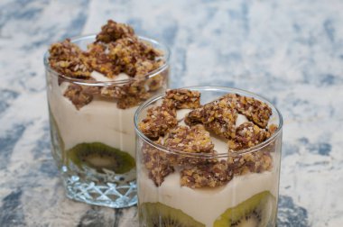 Granola, kivi, muz ve yunan yoğurt gri beton üzerinde iki bardak