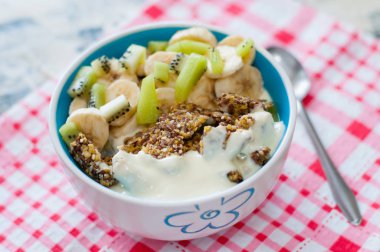 Granola Yunan yoğurt kivi ve muz ile kase de pembe bir peçete üzerinde bir kaşık, üstten görünümü. Kilo kaybı, uygun ve lezzetli gıda için Fitness diyet